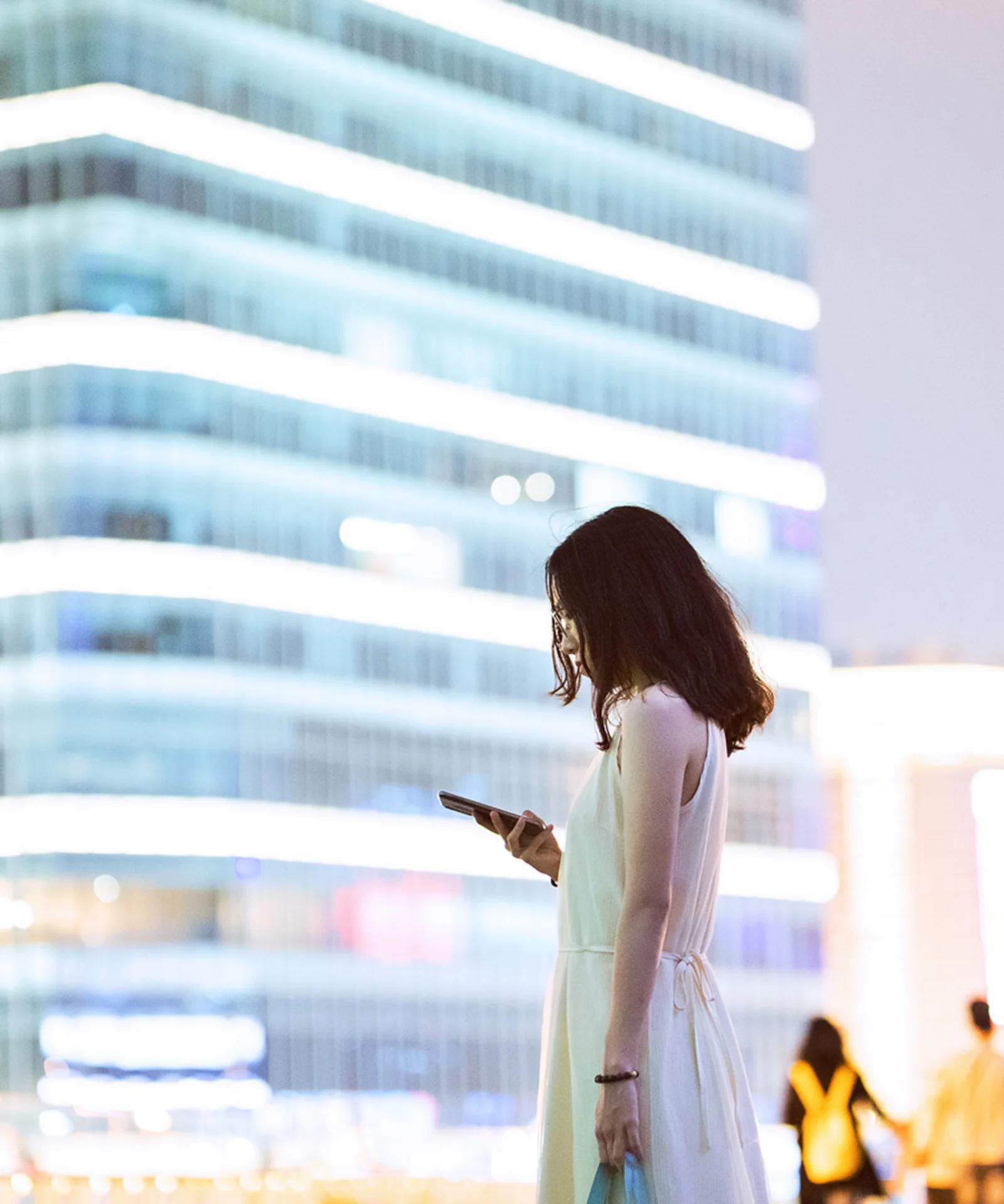 A professional woman using her smartphone with a modern cityscape in the background, symbolizing the impact of Central Bank Digital Currencies (CBDCs) on the future of commercial banking.