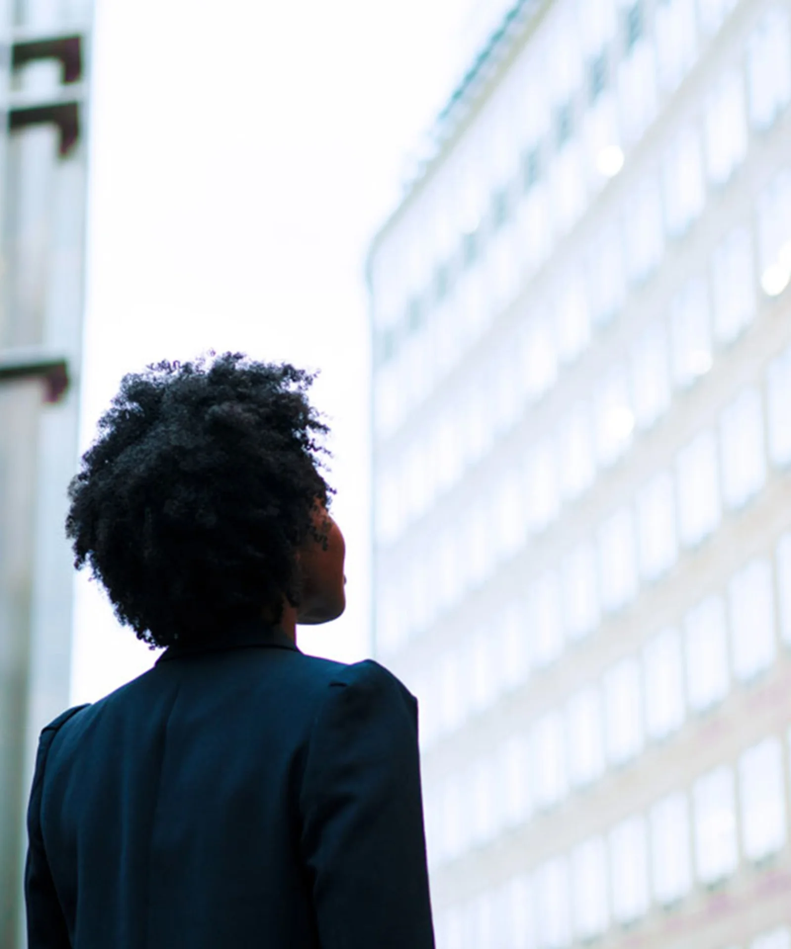 A business professional looking up at modern office buildings, illuminated with vibrant lights in an urban setting.