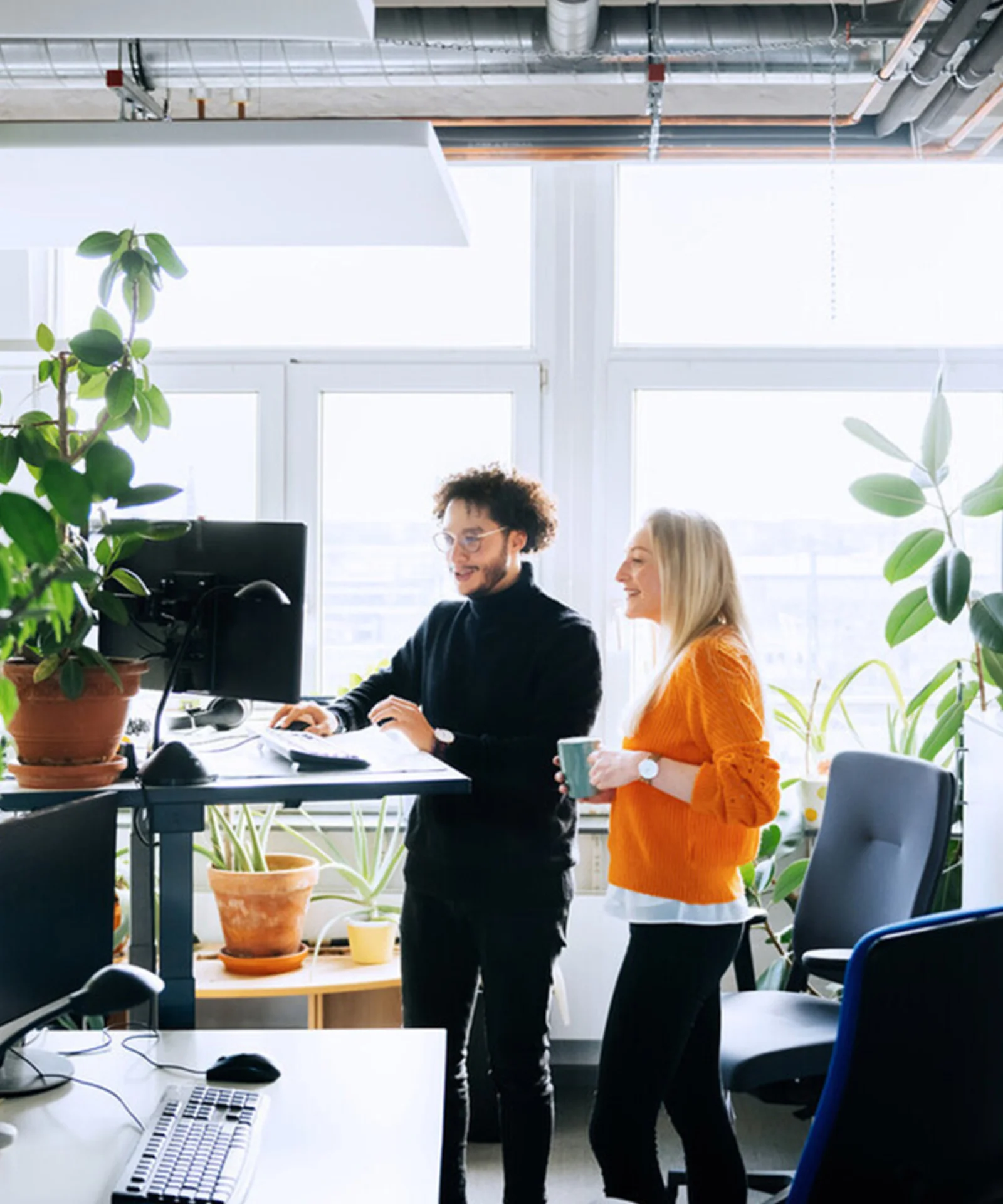 Two employees in a bright, plant-filled office space, representing GFT&#039;s commitment to sustainability and its improved CDP Climate Change rating.