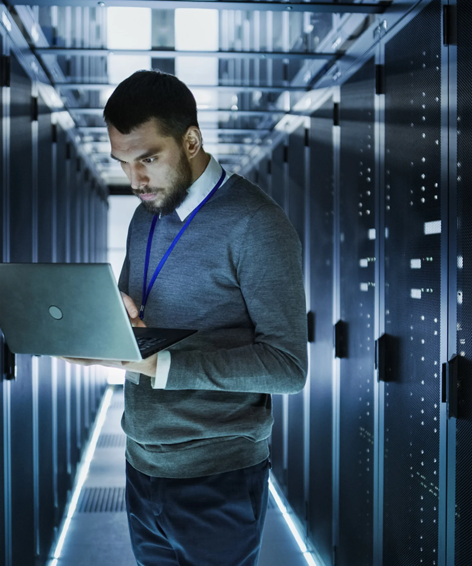 An IT professional working on a laptop in a high-tech server room, surrounded by rows of data servers.