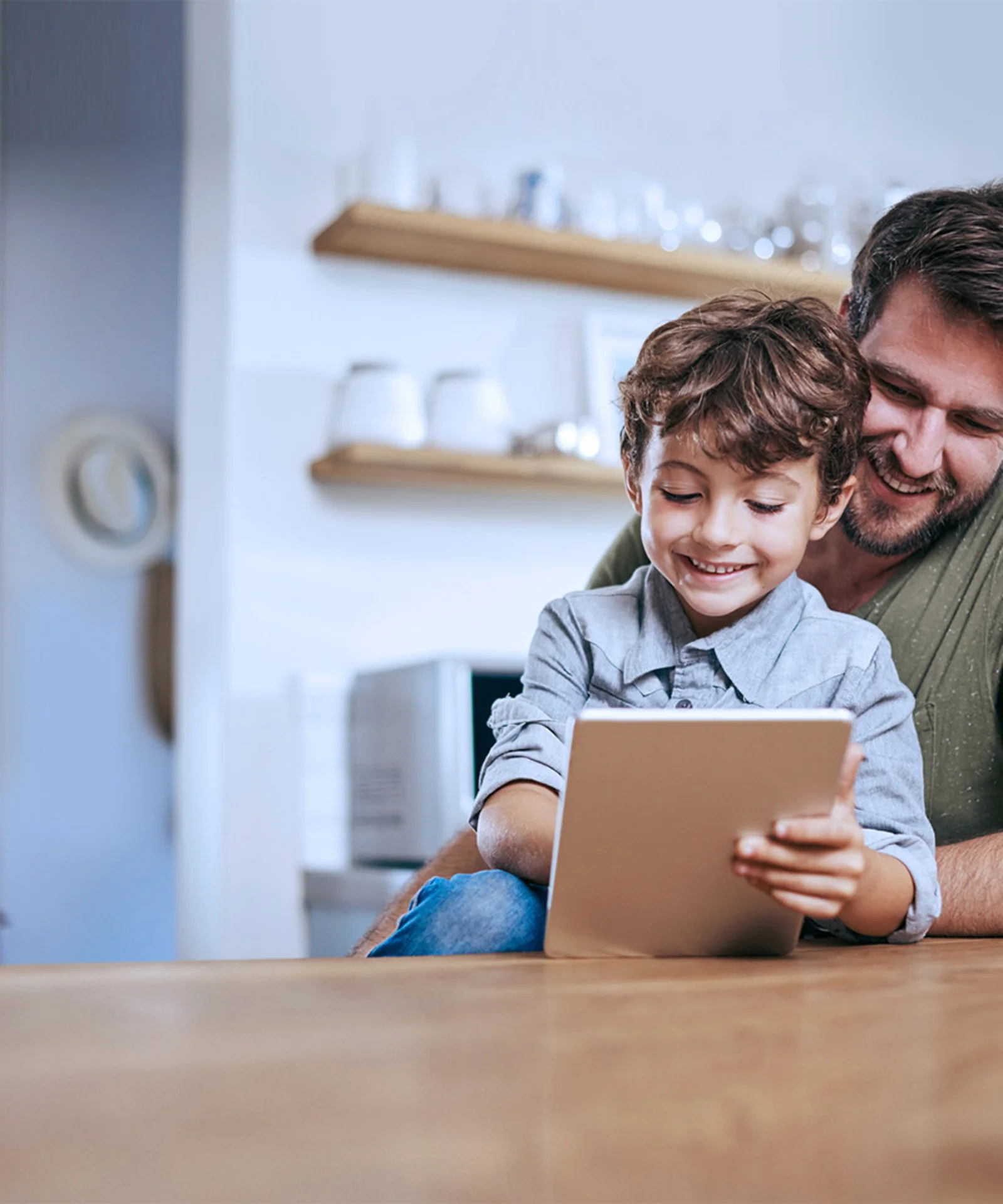 A smiling father and his young son enjoying time together using a tablet, illustrating a digital platform designed for children.