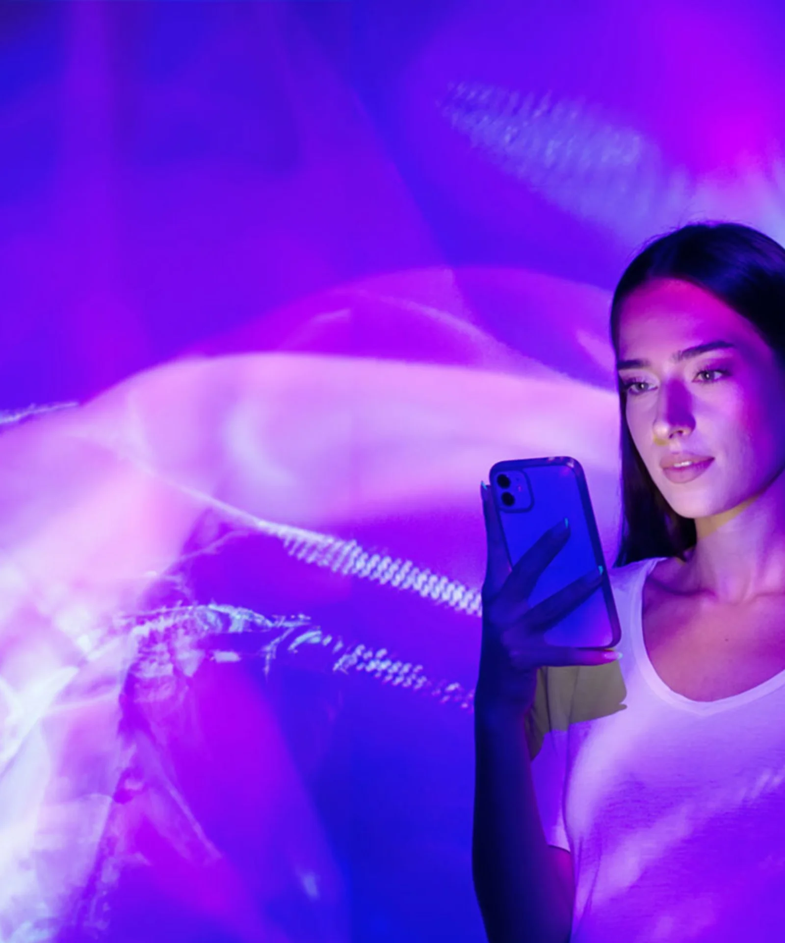 This key visual for GFT Banking Agent showcases a woman holding a smartphone, enveloped in a mesmerizing display of abstract purple and pink lights. The image evokes a sense of modern technology and digital innovation, reflecting the dynamic and futuristic nature of the GFT Banking Agent. The interplay of lights and shadows creates an immersive and visually captivating atmosphere, symbolizing the seamless integration of advanced AI and banking technology in enhancing customer experiences.