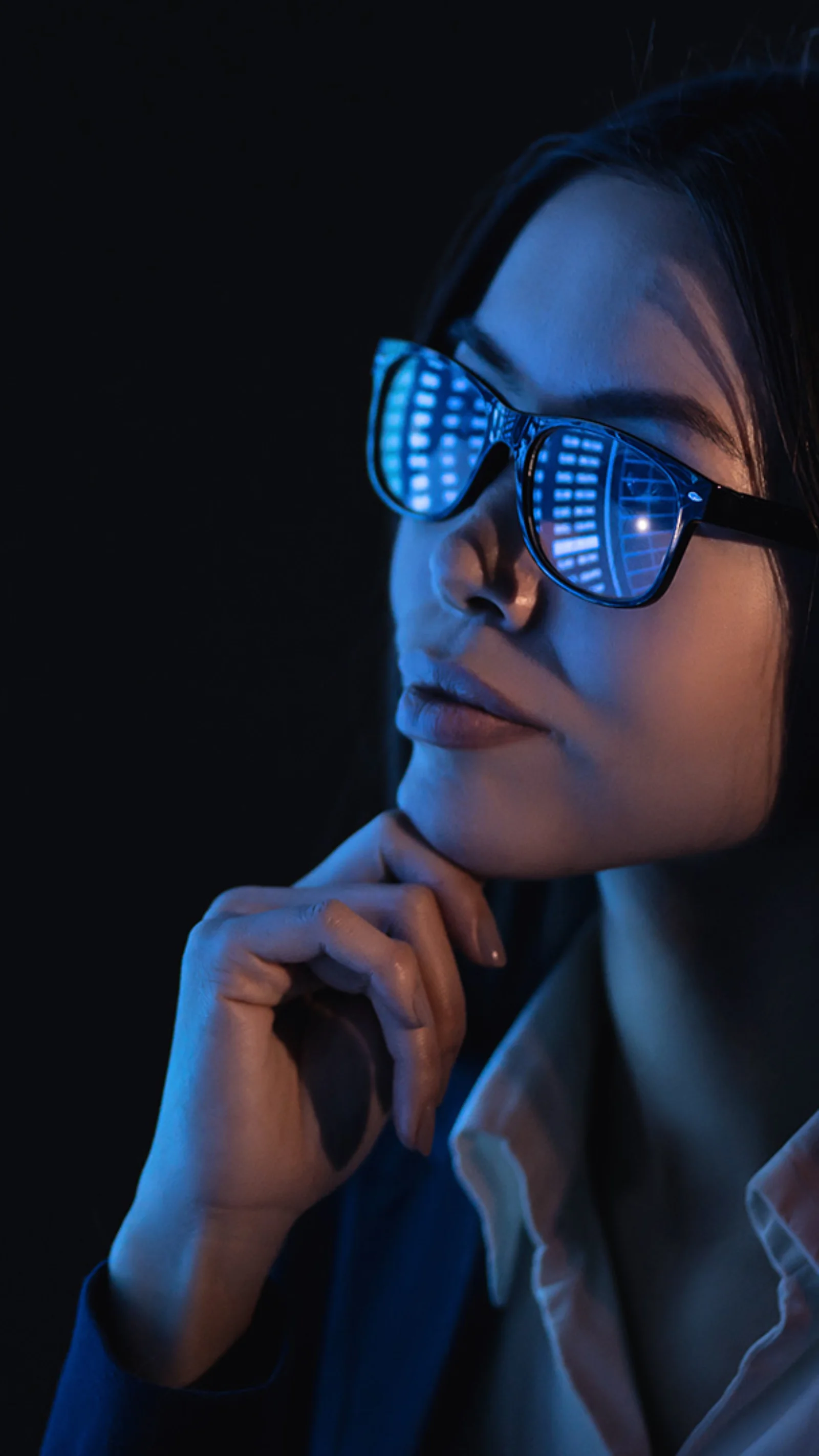 Una mujer con gafas, reflejando gráficos de datos, mira atentamente varias pantallas digitales que muestran diversos análisis y gráficos.