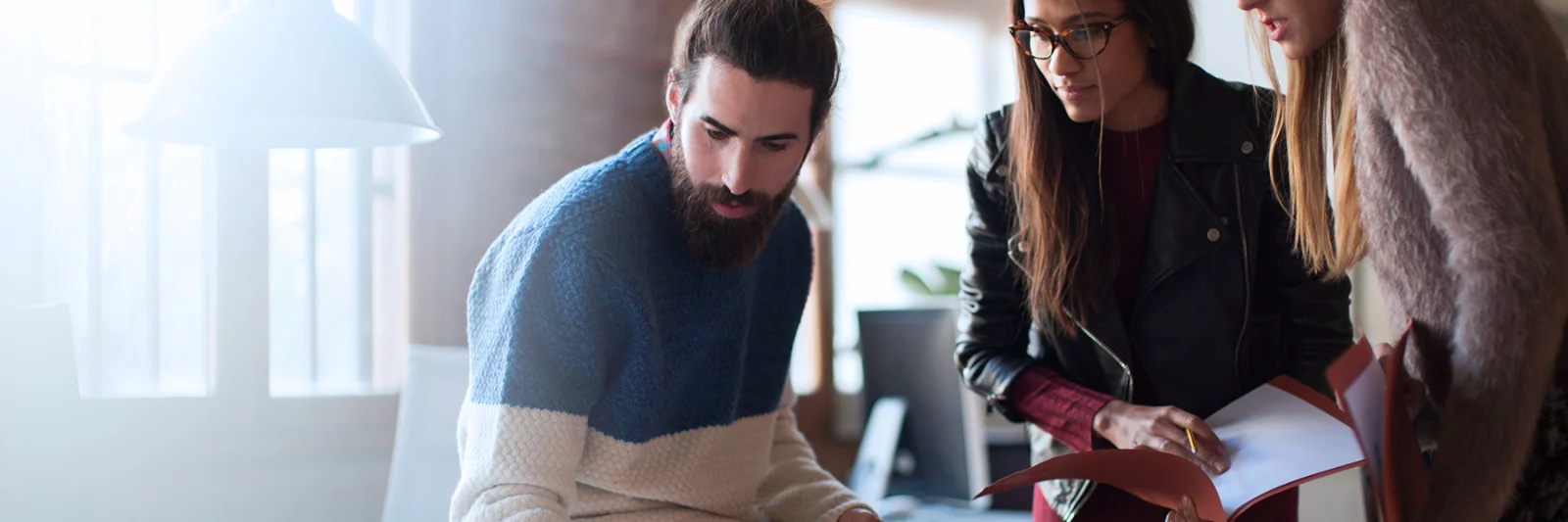 Three professionals collaborating around a laptop, symbolising the partnership between GFT and 10x Banking to drive innovation in the financial services sector.