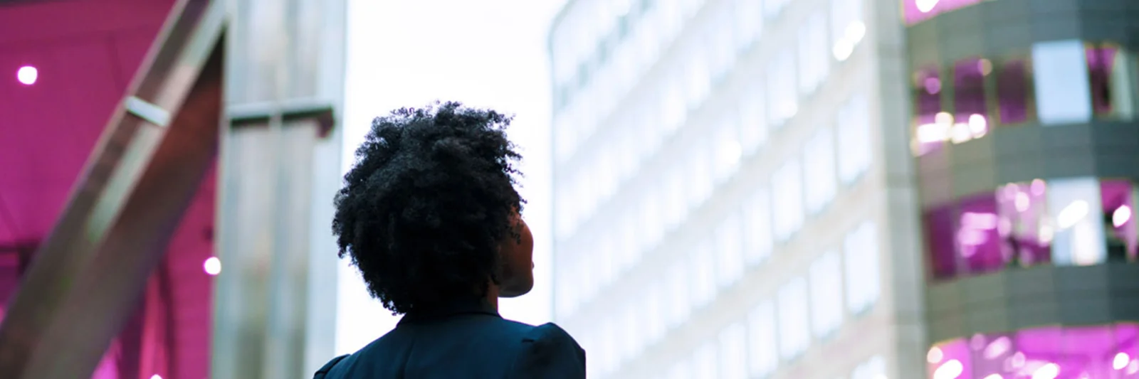 A business professional looking up at modern office buildings, illuminated with vibrant lights in an urban setting.