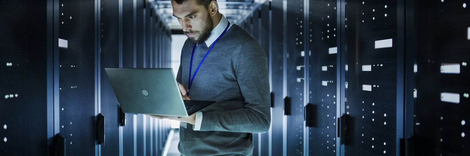 An IT professional working on a laptop in a high-tech server room, surrounded by rows of data servers.