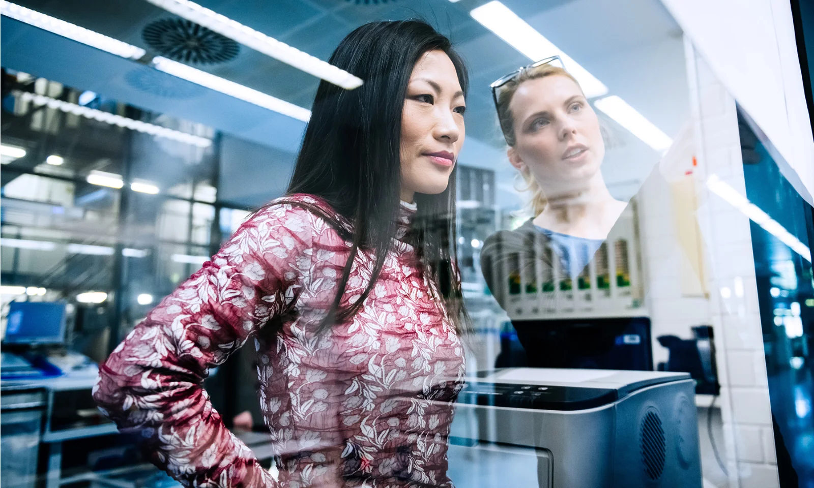 Two professionals collaborating on a project, with a woman in a floral top intently focusing on the task at hand in a modern office or lab setting.