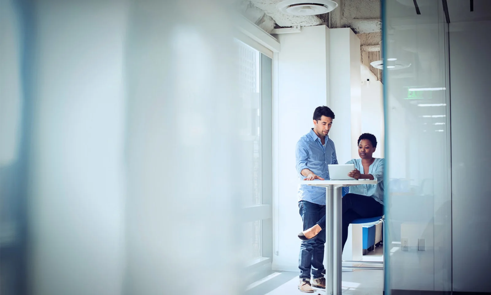 Two colleagues working together in a bright, modern office, reviewing information on a tablet while standing at a high desk.