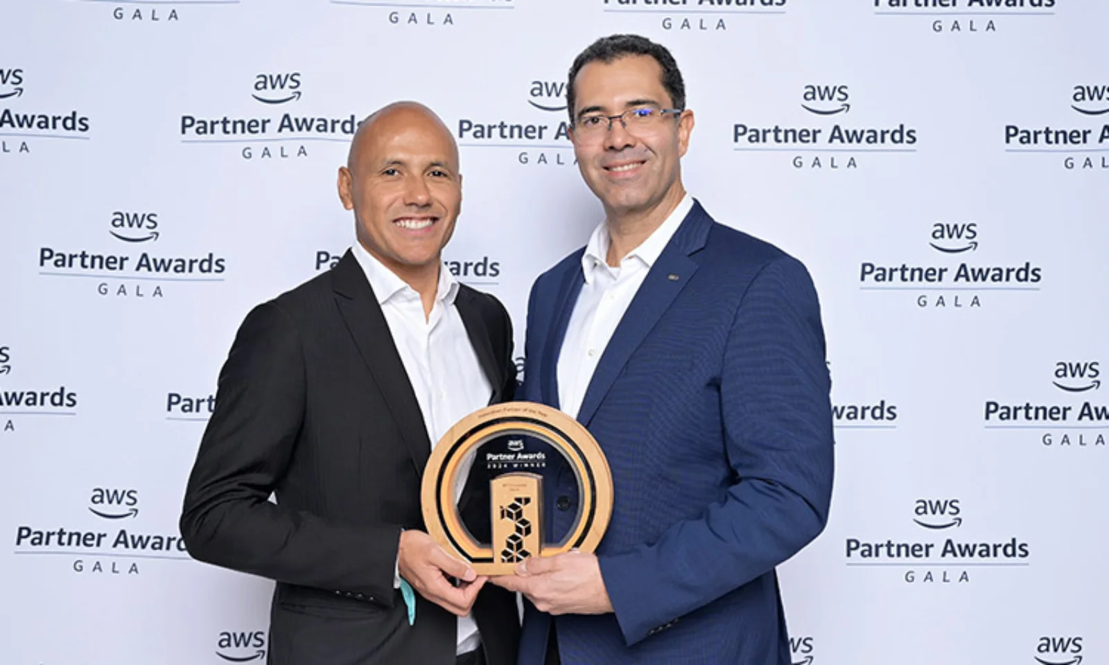 Marco Santos and Carlos Kazuo holding an award at the AWS Partner Awards Gala, standing in front of a branded backdrop celebrating AWS Partner achievements.