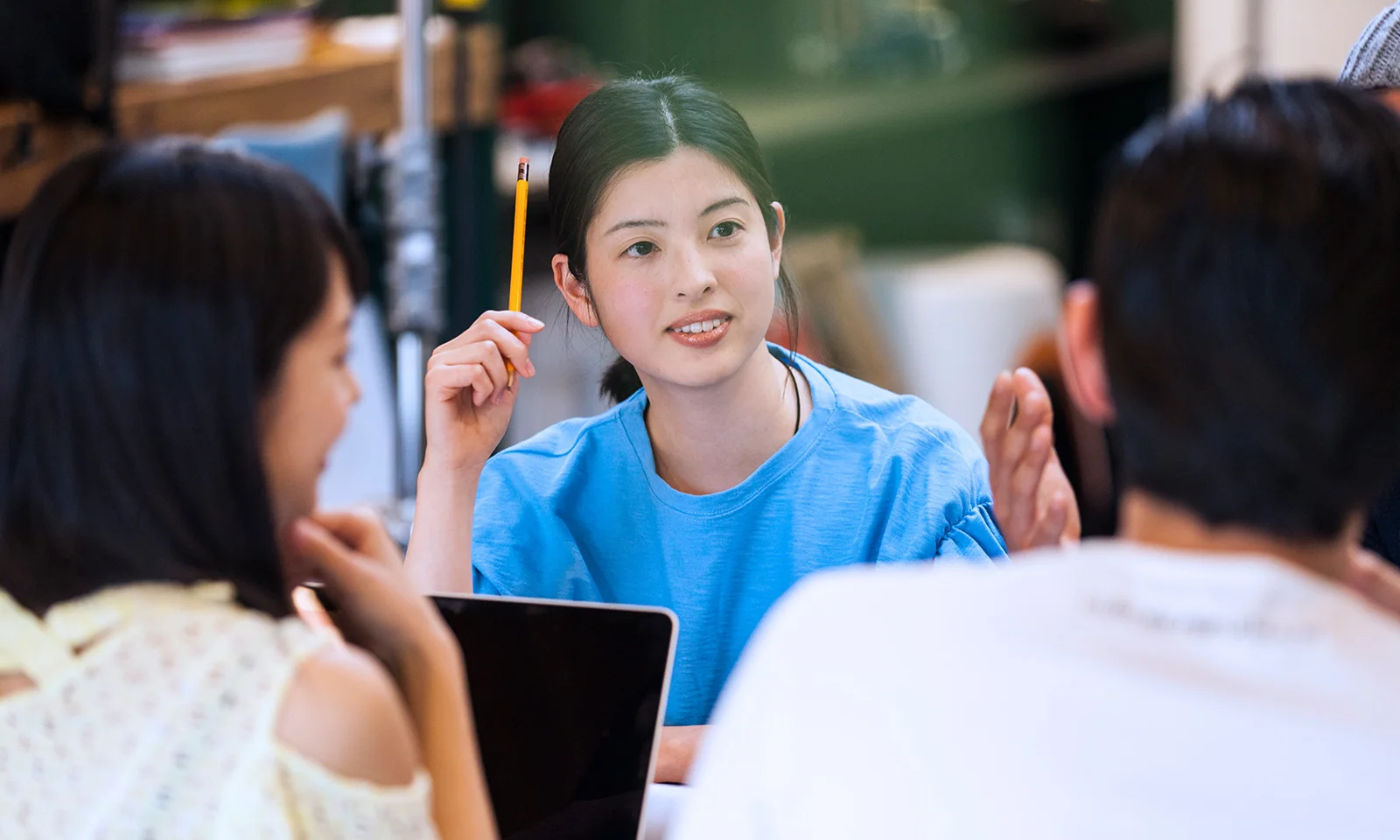 Young professional woman holding a pencil, engaged in a collaborative discussion with colleagues in a modern workspace.