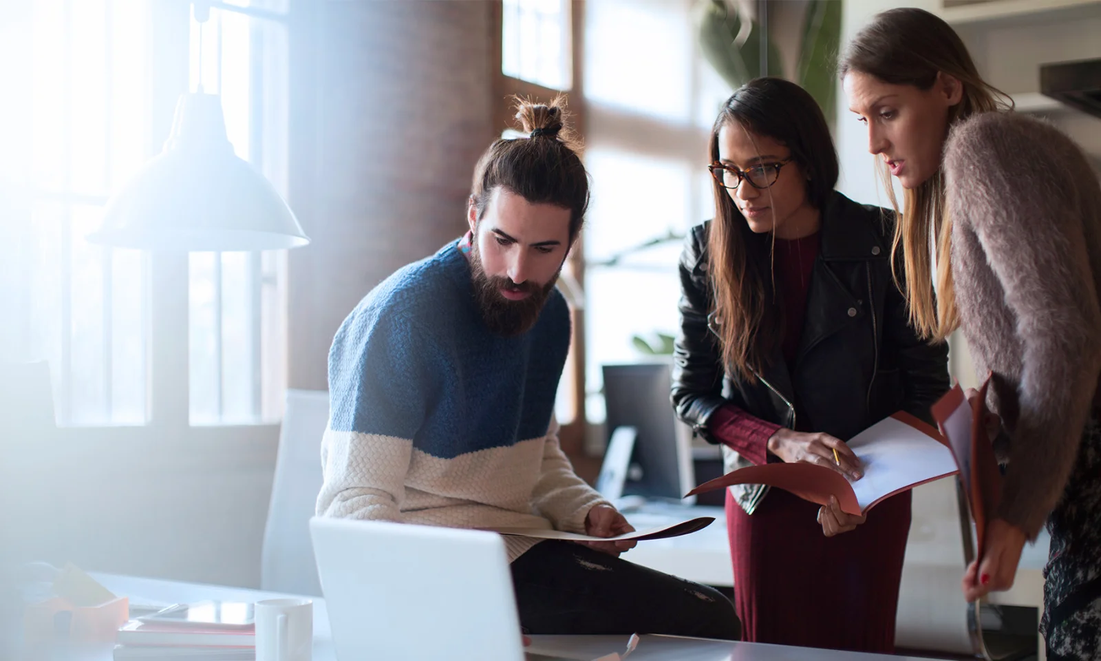 Tres profesionales colaboran alrededor de una computadora portátil, simbolizando la asociación entre GFT y 10x Banking para impulsar la innovación en el sector de servicios financieros.