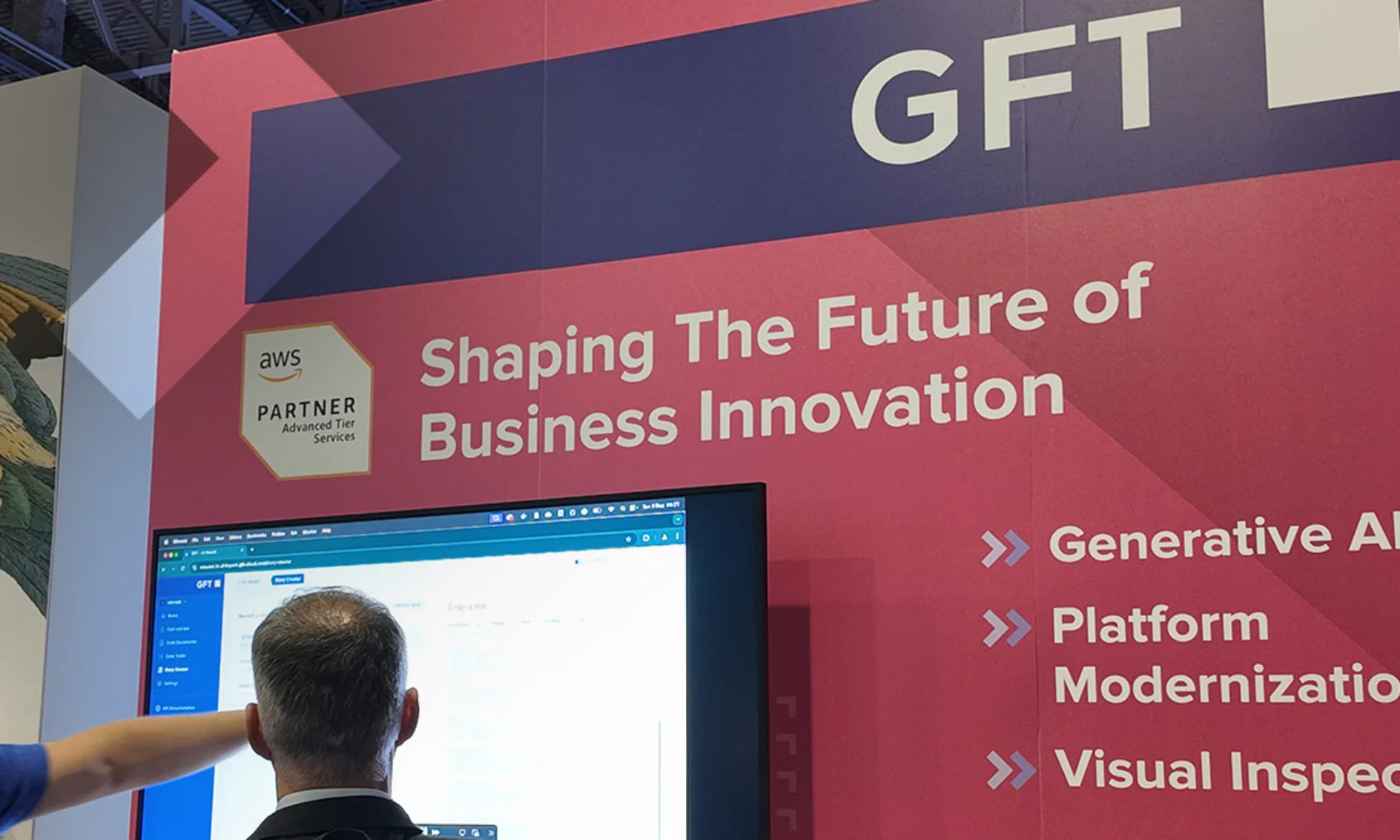 GFT exhibition booth with a banner reading &quot;Shaping the Future of Business Innovation,&quot; highlighting services such as Generative AI, Platform Modernization, and Visual Inspection. Two individuals are interacting with a screen showcasing GFT technology solutions.