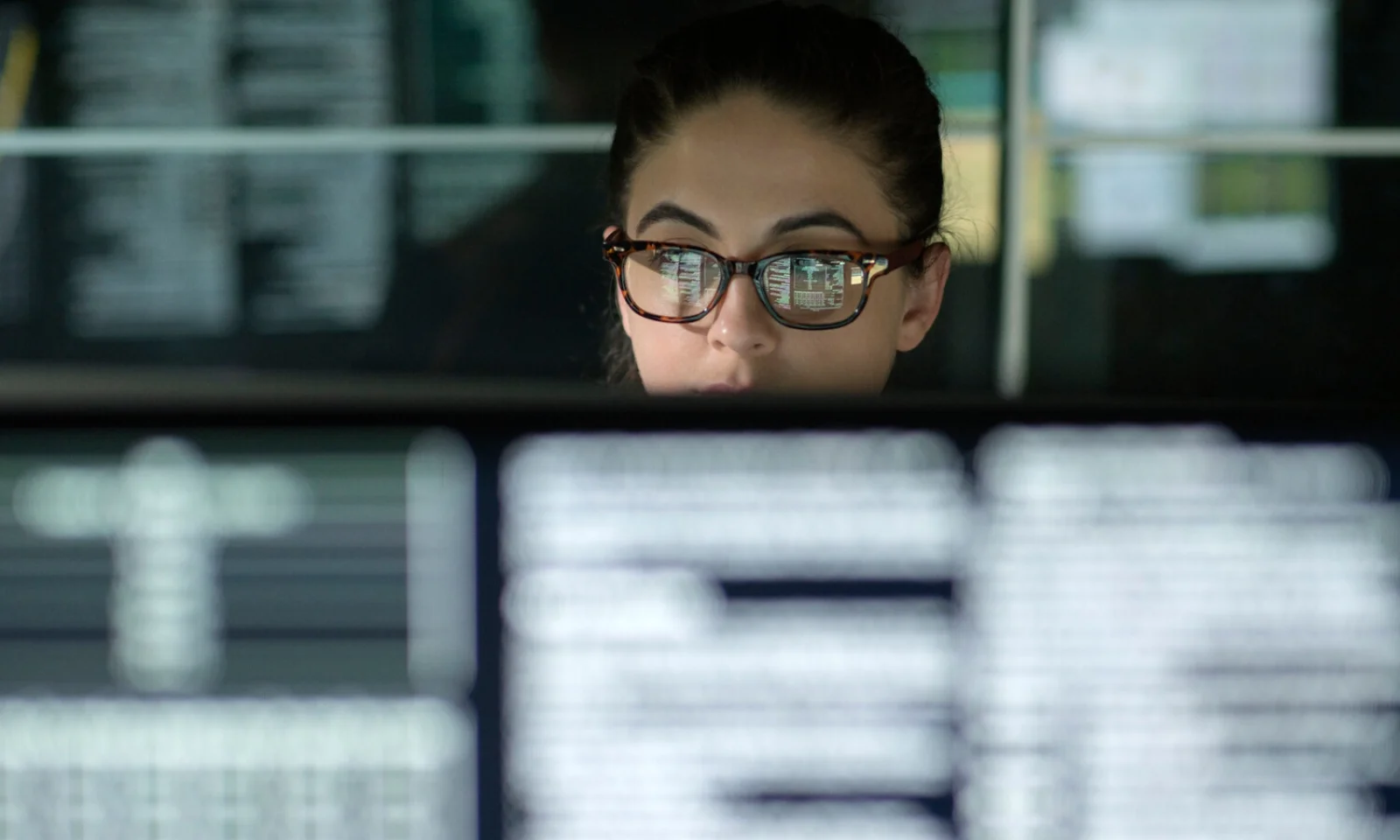 Una persona que usa gafas con código de computadora reflejado en las lentes, sentada frente a múltiples pantallas llenas de líneas de código, que representan el entorno técnico e innovador de AWS Windows.