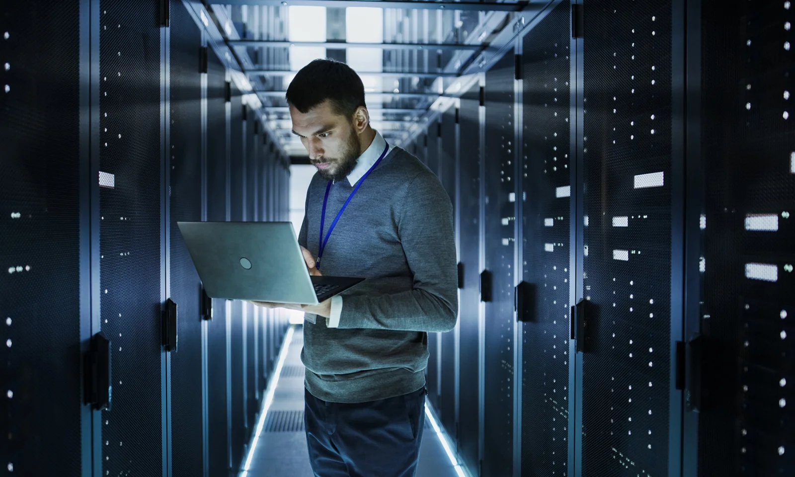 An IT professional working on a laptop in a high-tech server room, surrounded by rows of data servers.