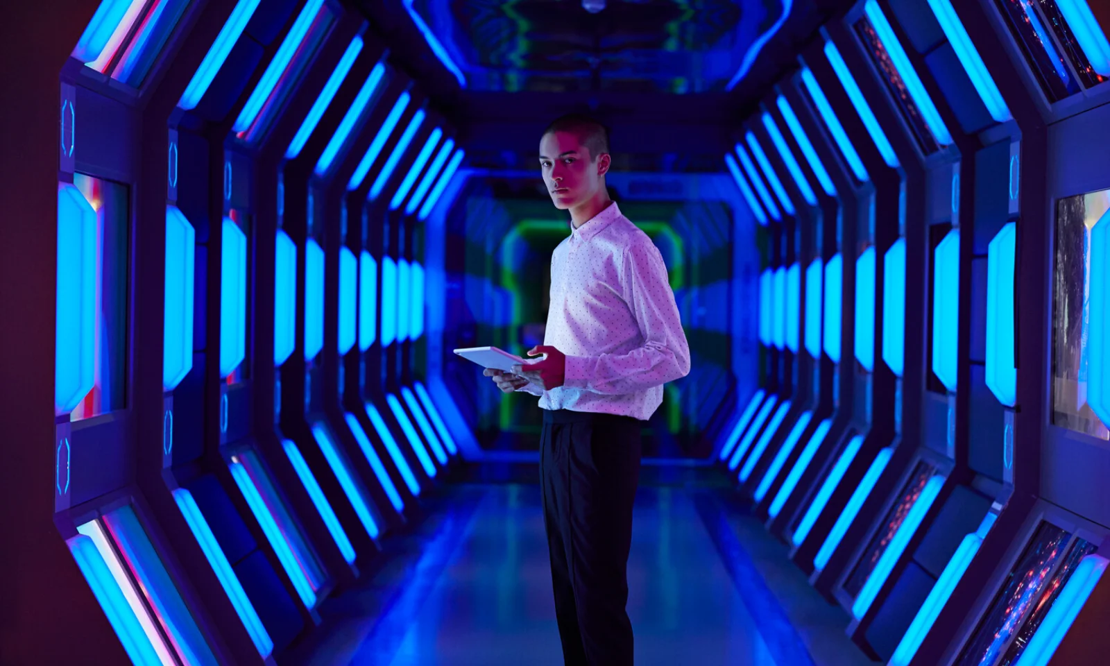 A person holding a tablet standing in a futuristic hallway with vibrant blue lighting, representing the advanced and innovative environment of AWS Kubernetes.