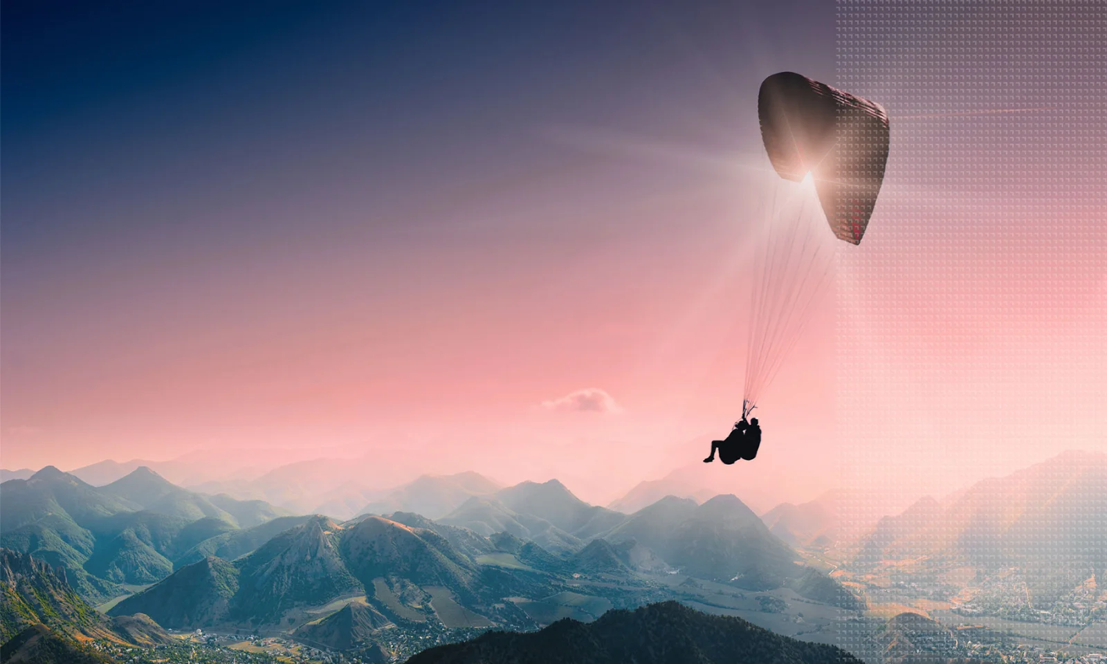 A paraglider silhouetted against a pink and blue sky, soaring over a mountainous landscape at sunrise.