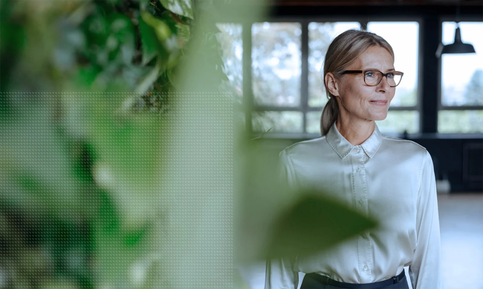 A professional woman in glasses and a white blouse standing confidently in an office environment with green plants, symbolizing GFT&#039;s commitment to corporate governance and ethical leadership.