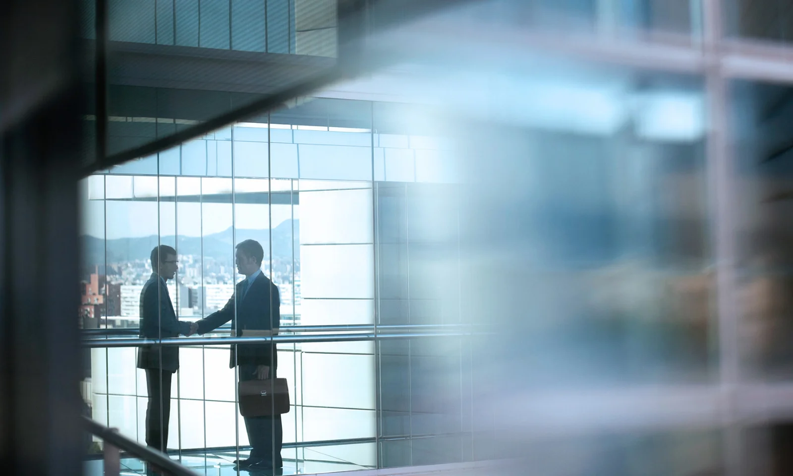 A key visual for IBM, featuring two business professionals shaking hands in a modern office building with a cityscape in the background. This image represents IBM&#039;s commitment to building strong partnerships and delivering innovative technology solutions. Discover how IBM&#039;s advanced technologies, in collaboration with GFT, can drive digital transformation and enhance your business operations.