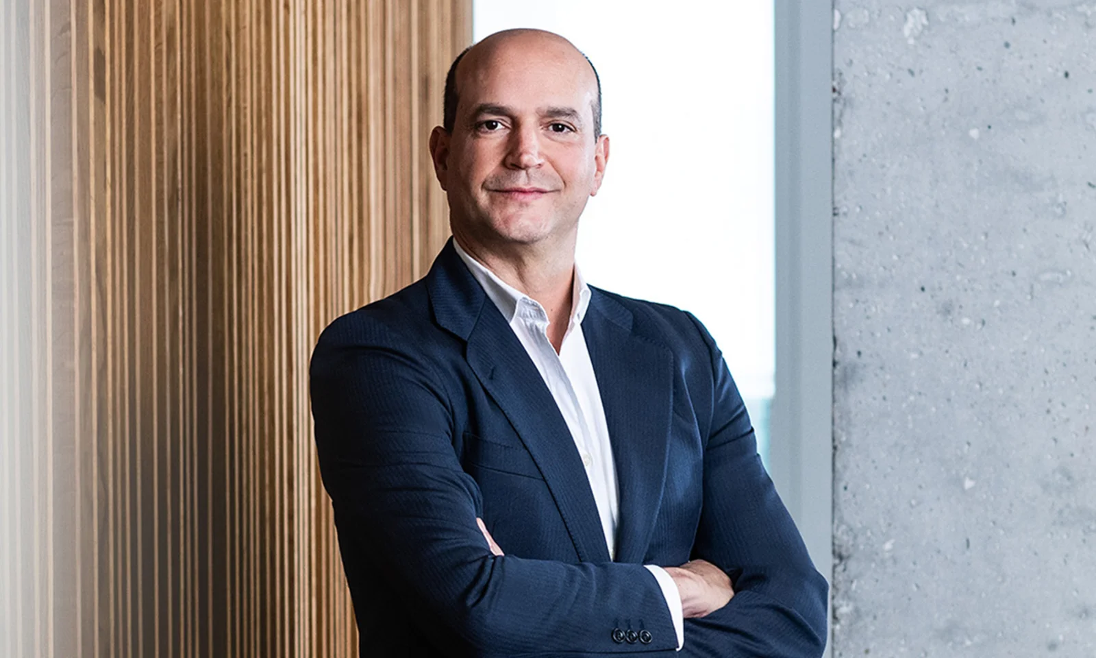 Professional portrait of Manuel Lavin, wearing a dark suit with arms crossed and a confident smile.