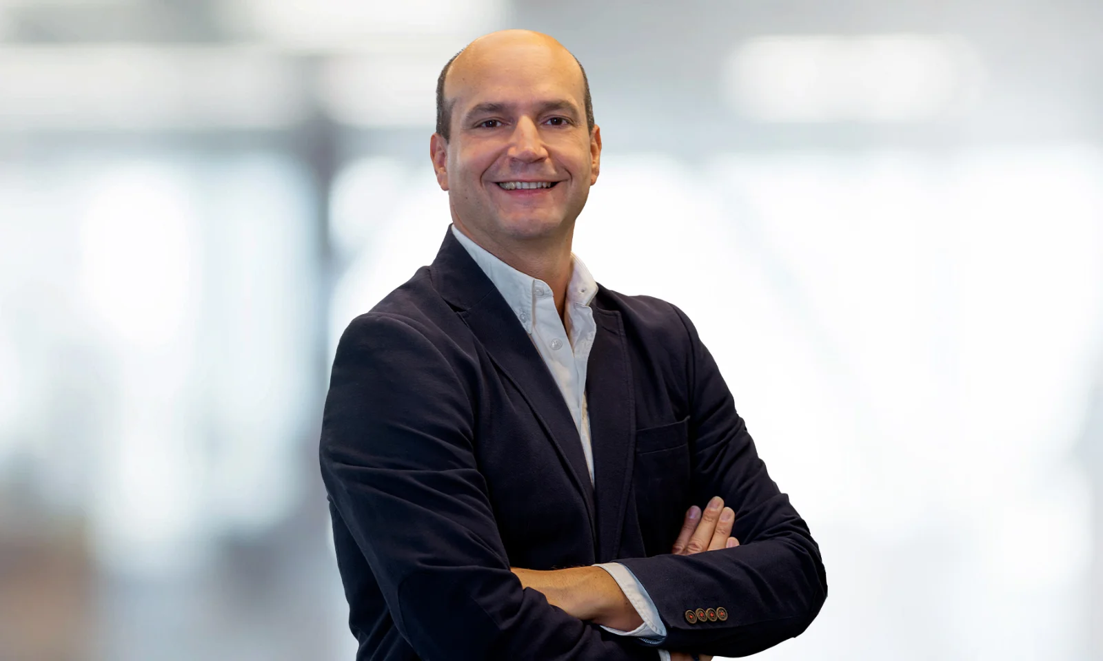 Professional portrait of Manuel Lavin, wearing a dark suit with arms crossed and a confident smile.