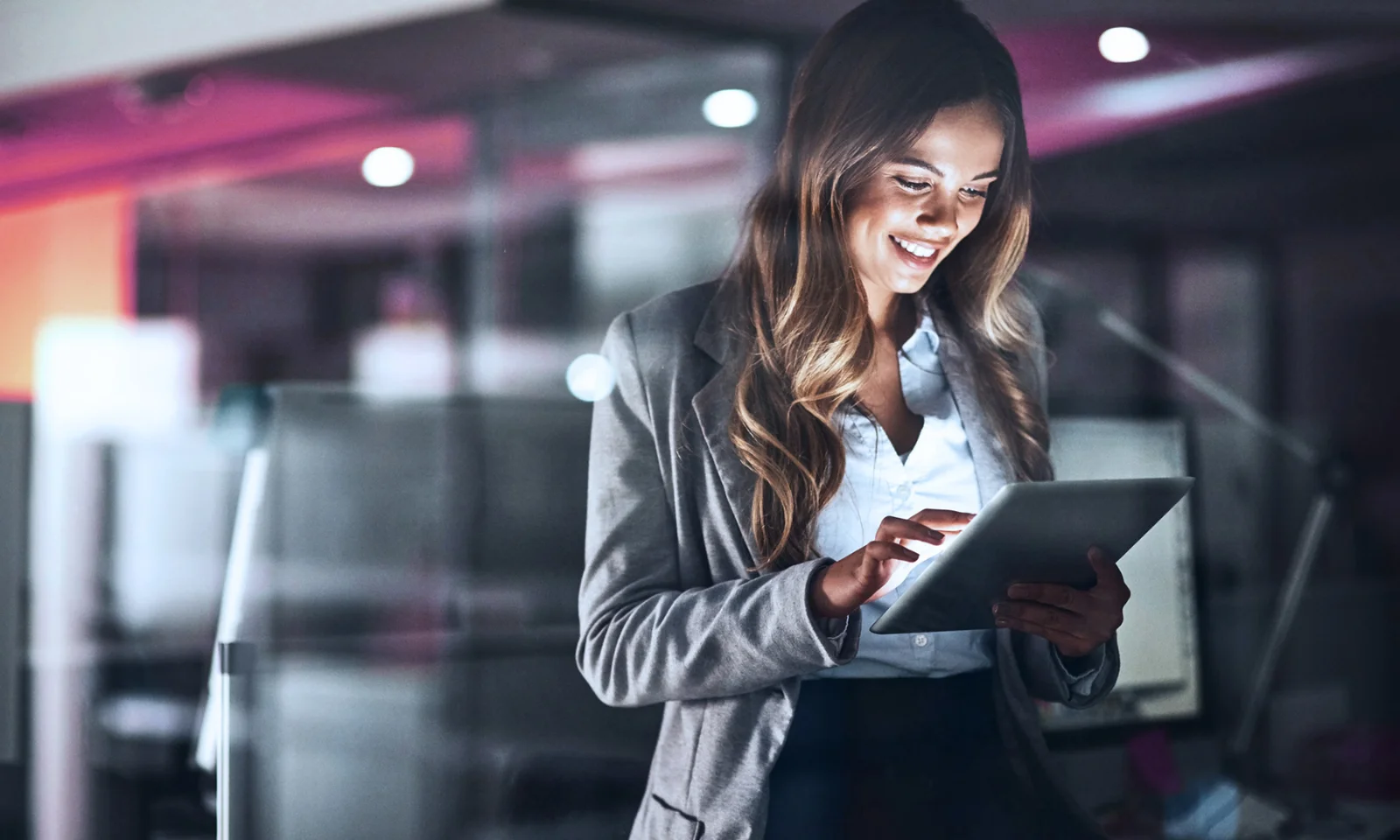 A businesswoman smiling while using a tablet in a modern office environment, representing the power of mobile technology and digital transformation in business.