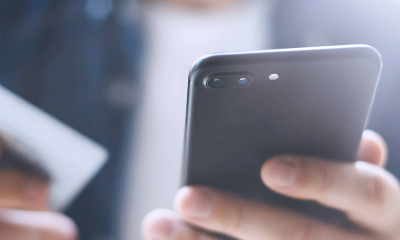 Close-up of a man holding a smartphone in one hand and a credit card in the other, representing mobile payment and online shopping.