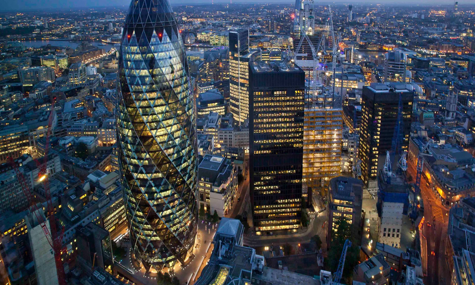 Aerial view of a cityscape at night, featuring illuminated skyscrapers including the Gherkin.