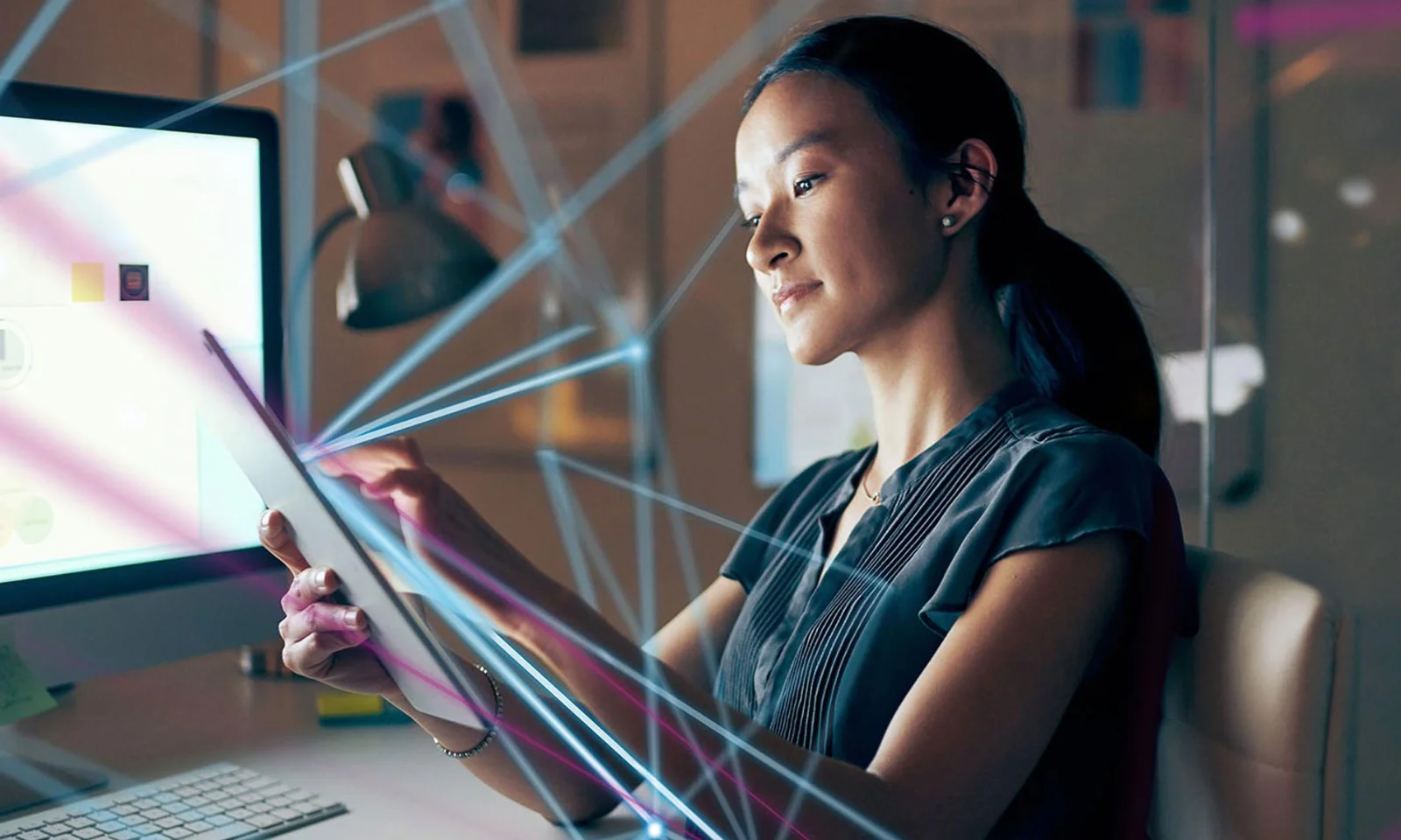 The image showcases a woman intently using a tablet in a sophisticated digital workspace, with multiple digital connections and data points illustrated around her. A computer monitor and office desk setup are visible in the background, emphasizing the integration of advanced technology in capital markets. The environment is bathed in cool tones, highlighting the data-driven and analytical nature of the capital markets sector. This visual represents the dynamic and interconnected world of capital markets, where technology and data play a pivotal role in decision-making and operations.