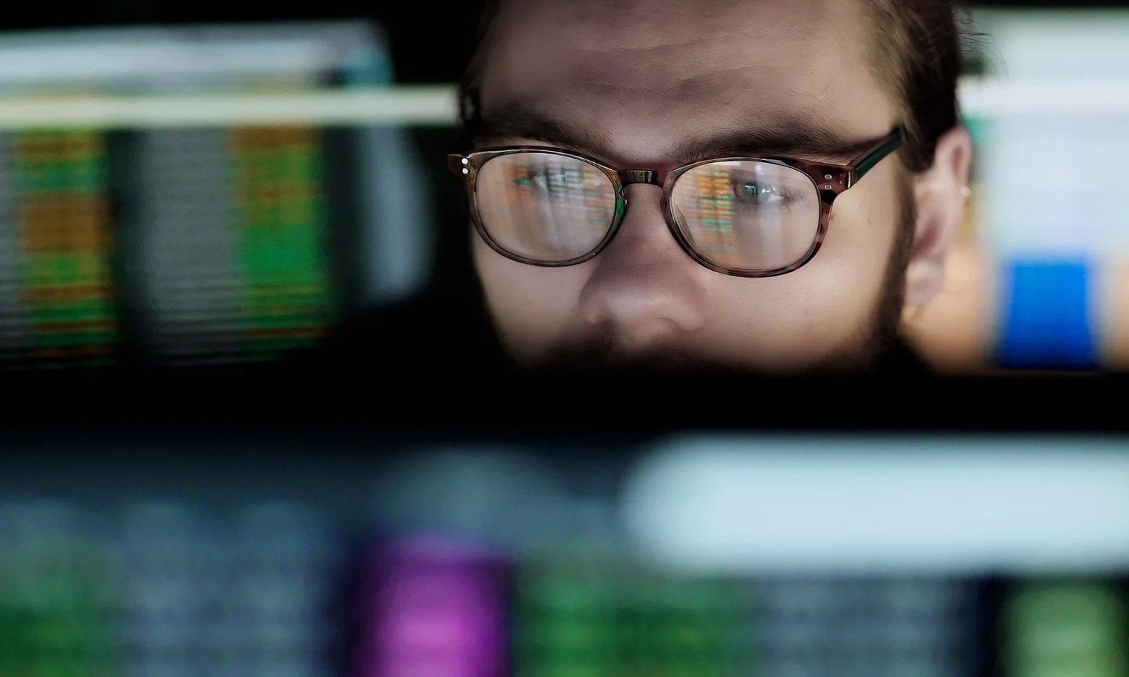 Close-up of a man wearing glasses, reflecting computer screens filled with data, representing the focus on machine learning operations (MLOps) in data-driven environments.