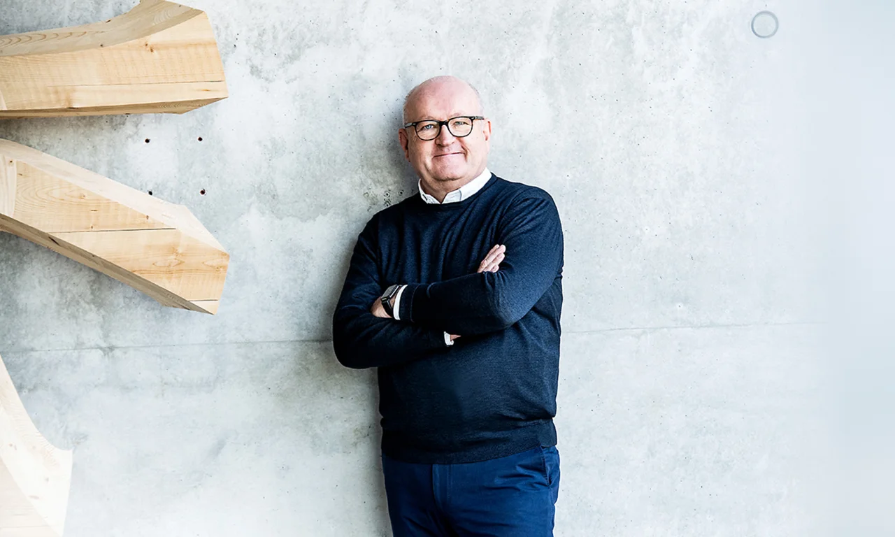 Ulrich Dietz standing confidently against a concrete wall, arms crossed, in a modern setting